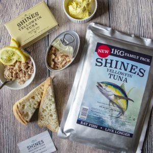 Shines Gourmet Yellowfin Tuna 1kg Family pouch shown on a rustic grey wooden table, alongside an opened pouch with tuna, lemon, butter, and bread slices.