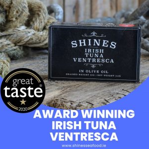Shines Irish Tuna Ventresca in olive oil sits on wood next to a rope, featuring a "Great Taste 2020" award sticker. Discover more at www.shinesseafood.ie.