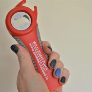 A hand with black and blue nails holds a red 5-in-1 Jar Opener featuring "WILD IRISH TUNA www.35ninesseafood.ie" branding against a plain background.