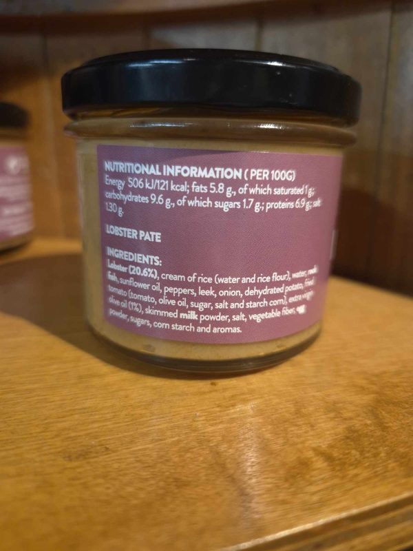A glass jar labelled "Shines Tuna PATE 100g" sits on a wooden shelf. Its label lists nutritional info and ingredients such as tuna, cream of rice, vegetables, oils, salt, and spices.