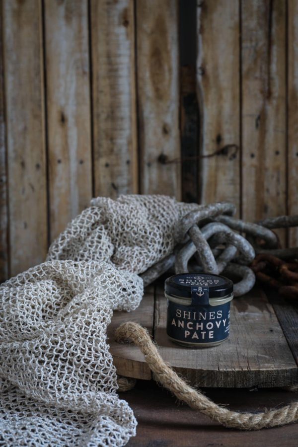 A Shines Pâté GIFT BOX (4 x 100g jars) rests on a wooden surface next to a fishing net, thick rope, and metal chain, with a rustic wooden backdrop.