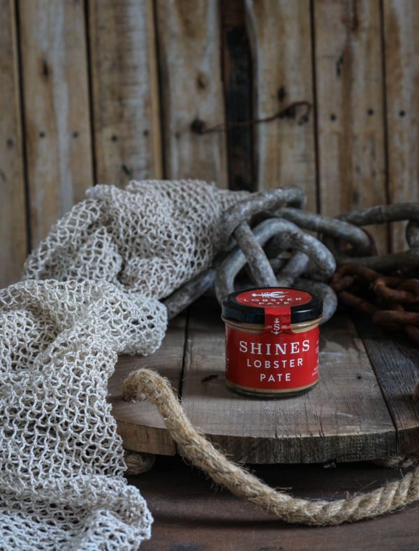 A Shines Pâté GIFT BOX containing 4 x 100g jars sits on a rustic wooden surface, surrounded by a fishing net, thick rope, and metal chain, against a wooden plank background.