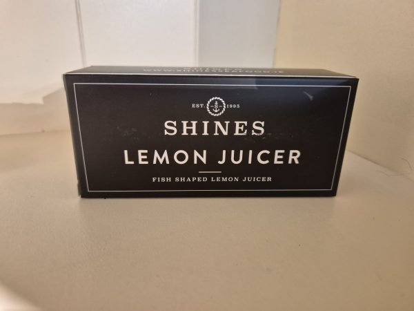 A black box labelled "Shines Lemon Juicer" with "Fish Shaped Lemon Juicer" printed below sits on a light surface.