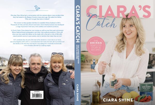 Book cover for Ciara's Catch Cook Book. Front: Ciara smiling in a kitchen with a forkful of food. Back: Ciara with two women outdoors, all in navy Shine’s Seafood jackets and sunglasses.